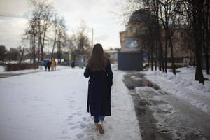 flicka promenader ner gata i vinter. kvinna i vinter- i stad. dålig väg i gård i Ryssland. foto