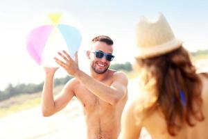 ung par spelar med en boll på de strand foto