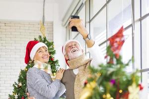 senior caucasian par fira jul tillsammans i lycka och spänning på Hem med röd santa hatt och jul träd foto