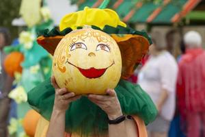 kreativt dekorerad halloween pumpor i mänsklig händer. en snäll ansikte med en leende målad på en pumpa. karneval kostym för de höst Semester. foto