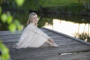 skön ung blond kvinna på en trä- bro nära de flod poserar, ser på de kamera. foto
