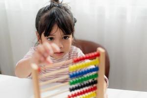 en ung söt asiatisk tjej använder kulramen med färgade pärlor för att lära sig att räkna hemma foto