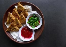 samosa, Samsa eller somsa är triangel- friterad bakverk eller bakverk eras med tomat sås och purjolök skiva, på svart bakgrund foto