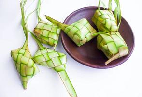 Ketupat i lergods tallrik isolerat på vit bakgrund. Ketupat ,ris klimp är mat eras när idhul Fitri eid mubarak i Indonesien, tillverkad från ris insvept i ung kokos löv, janur foto