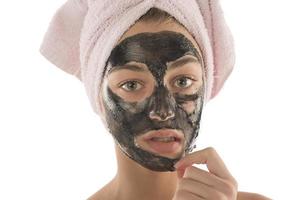 svart ansiktsbehandling mask. skön flicka pålning av svart mask. skönhet begrepp foto