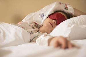trött kvinna sovande i säng bär blind- sömn mask foto