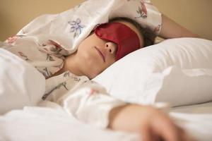 trött kvinna sovande i säng bär blind- sömn mask foto