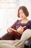 ung asiatisk kvinna kort hår läsa en bok i levande rum foto