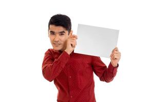 ung brunett man i röd t-shirt Framställ med vit plakat isolera på bakgrund foto