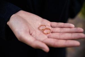 brudgum innehav bröllop ringar i hand. två bröllop ringar på de golv med kontrast bröllop ringar på golv, på jord, på piano, i hand foto