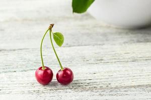 två röd körsbär med blad på en vit bakgrund foto