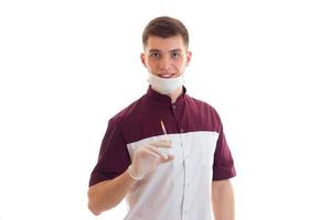 leende ung läkare med en mask på din ansikte håller sig de spruta med en vaccin isolerat på en vit bakgrund foto