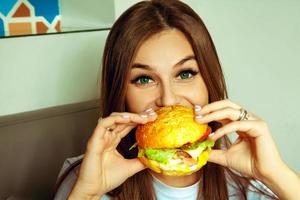 roligt brunett flicka äter hamburgare foto