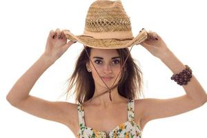 charmig ung brunett flicka med sugrör hatt och sommar kläder med blommig mönster ser på de kamera isolerat på vit bakgrund foto