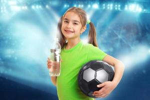 liten flicka med fotboll boll i händer drycker vatten foto