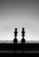 schack styrelse med schack bitar silhuetter på vit bakgrund. begrepp av företag idéer, konkurrens och strategi idéer. svart och vit klassisk konst Foto. kungar bekämpa i mitten. foto
