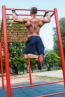 muskulös man håller på med pull-ups på horisontell bar foto