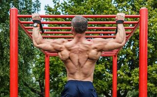 muskulös man håller på med pull-ups på horisontell bar foto