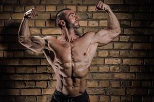 kroppsbyggare som visar hans muskler mot tegel vägg foto