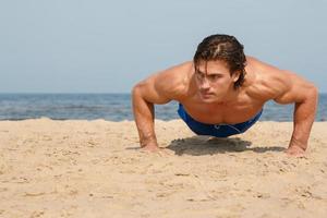 muskulös man under hans träna på de strand foto