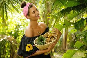 Lycklig ung kvinna med en korg full av exotisk frukt foto