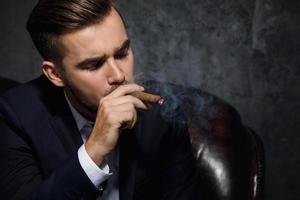 porträtt av stilig rik man är rökning cigarr foto