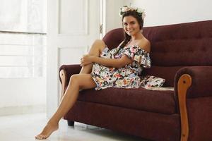 Lycklig kvinna i skön klänning är Sammanträde på de årgång soffa foto