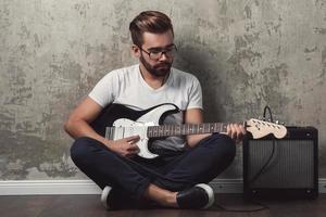 eleganta skäggig kille med gitarr mot betong vägg foto