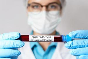 kvinna läkare är innehav en blod prov av de SARS-CoV-2 foto