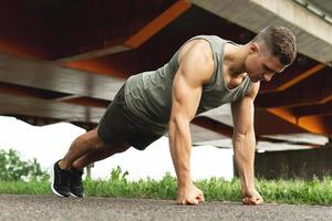 muskulös man är håller på med armhävningar under calisthenic träna på en gata foto