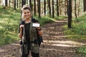 kvinna vandrare som visar smartphone med tom visa i grön skog foto