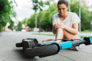 ung kvinna lidande från knä smärta efter e-skoter ridning olycka foto