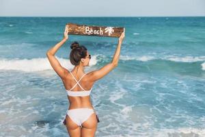 sexig kvinna bär baddräkt med gammal trä- tecken på de strand foto