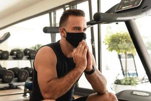 ung atletisk man bär en förebyggande ansikte mask under hans träna i de Gym foto