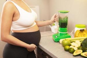 gravid kvinna göra en grön friska smoothie på Hem foto