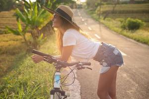 kvinna med en cykel på smal Land väg foto