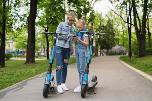 mor och dotter använder sig av Ansökan på smartphone för delning elektrisk skotrar foto