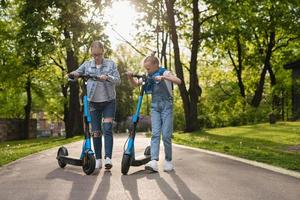 mor och dotter ridning elektrisk skotrar i stad parkera foto