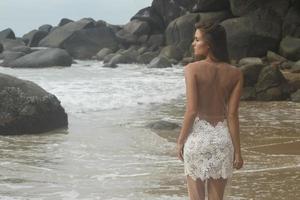 ung kvinna bär skön vit klänning är Framställ på de strand foto