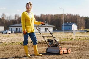 kvinna bybo är använder sig av luftare maskin till förskärning och luftning av gräsmatta eller äng foto