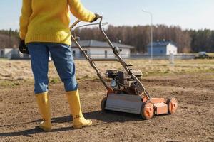 kvinna bybo är använder sig av luftare maskin till förskärning och luftning av gräsmatta eller äng foto