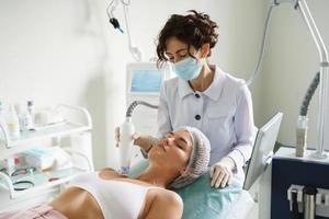 läkare och kvinna klient under radiofrekvens lyft behandling i en medicinsk estetisk klinik foto