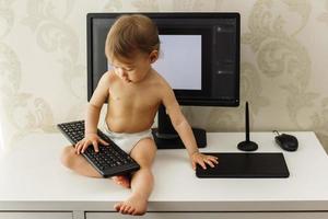 liten pojke Sammanträde på en skrivbord och spelar med en tangentbord. foto