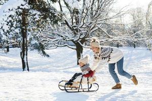 mor och henne söt liten son har på en sledding kulle under solig vinter- dag foto