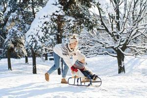 mor och henne söt liten son har på en sledding kulle under solig vinter- dag foto