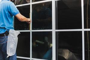 arbetstagare använda sig av skrapa rengöring fönster innan montera toning filma. foto