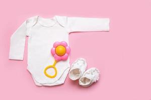 kroppsdräkt, skallra och tossor för en nyfödd på en rosa bakgrund foto