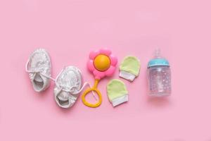 Tillbehör för en nyfödd - tossor, en skallra, vantar och en flaska för formel på en rosa bakgrund foto