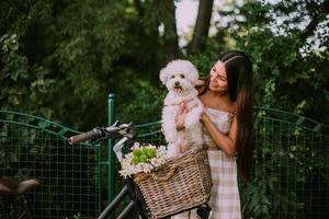 ung kvinna med vit bichon frise hund i korgen med elcykel foto