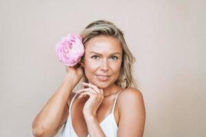 skönhet porträtt av blond hår leende ung kvinna med rosa pion i hand isolerat på vit bakgrund foto